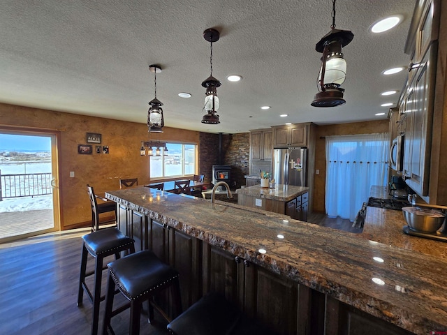 kitchen featuring dark hardwood / wood-style flooring, dark stone counters, a textured ceiling, a breakfast bar area, and appliances with stainless steel finishes