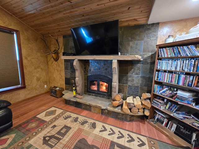 living room featuring hardwood / wood-style floors, a stone fireplace, and wood ceiling