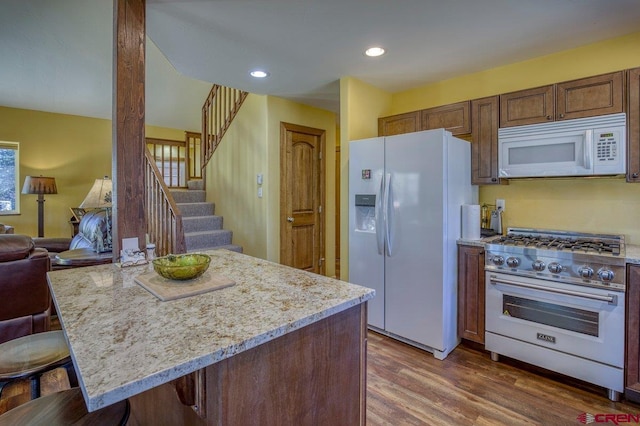 kitchen with a kitchen bar, white appliances, light stone counters, and dark wood-type flooring