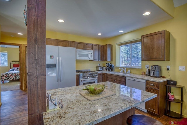 kitchen featuring white appliances, sink, light stone countertops, dark hardwood / wood-style flooring, and a kitchen bar