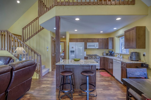 kitchen featuring dark hardwood / wood-style floors, a kitchen island, light stone countertops, and white appliances