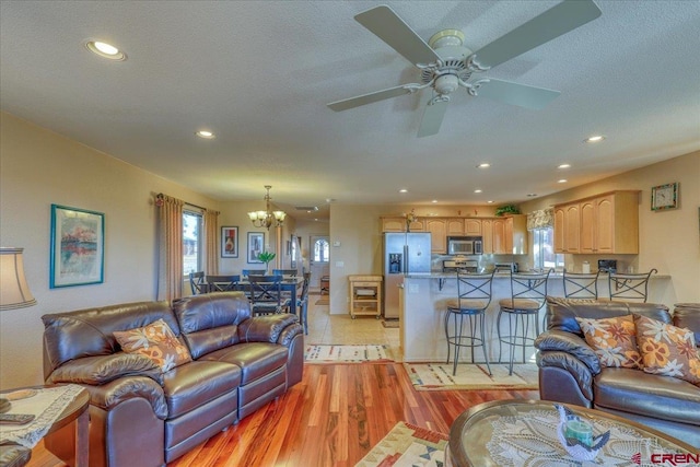 living room with ceiling fan with notable chandelier, light hardwood / wood-style floors, and a textured ceiling