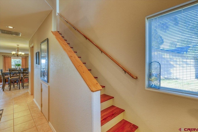 stairway with tile patterned floors and an inviting chandelier