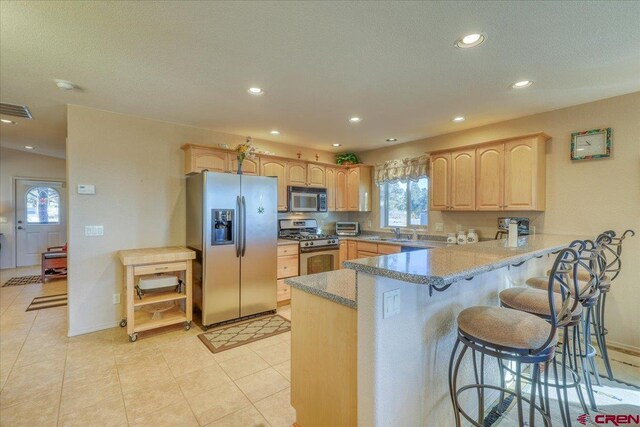 kitchen featuring light brown cabinets, sink, stainless steel appliances, a kitchen breakfast bar, and kitchen peninsula