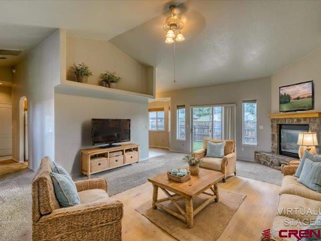 living room featuring a stone fireplace, a ceiling fan, and a healthy amount of sunlight