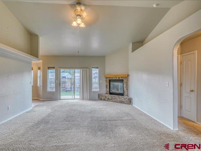 unfurnished living room featuring arched walkways, baseboards, a ceiling fan, carpet, and a stone fireplace