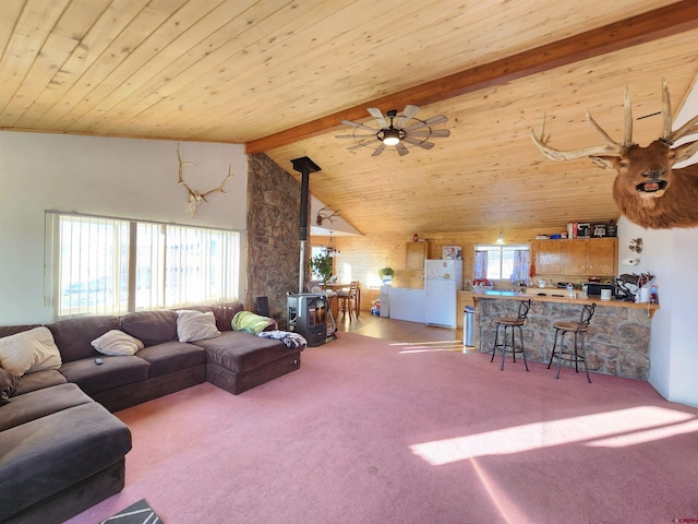 living room featuring vaulted ceiling with beams, carpet floors, a wood stove, and wooden ceiling