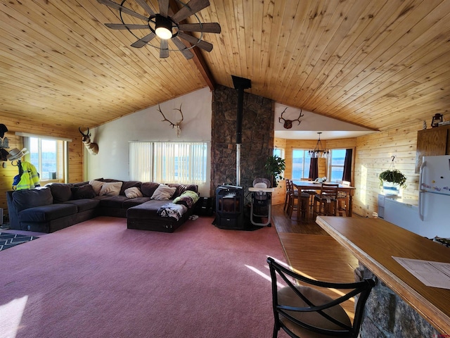 living room featuring a wood stove, plenty of natural light, ceiling fan with notable chandelier, and vaulted ceiling with beams