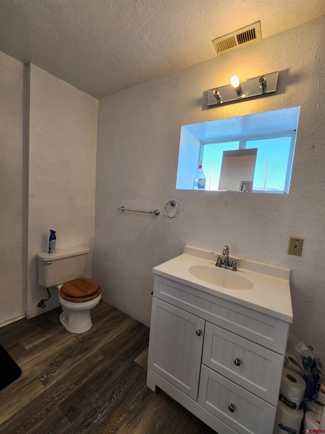 bathroom with hardwood / wood-style flooring, vanity, toilet, and a textured ceiling