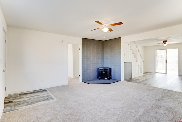 unfurnished living room featuring a wood stove, baseboards, a ceiling fan, and carpet flooring