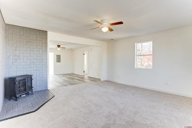 unfurnished living room featuring carpet floors, a ceiling fan, baseboards, electric panel, and a wood stove