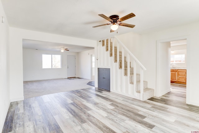 empty room with light wood-style floors, a ceiling fan, a sink, and stairs