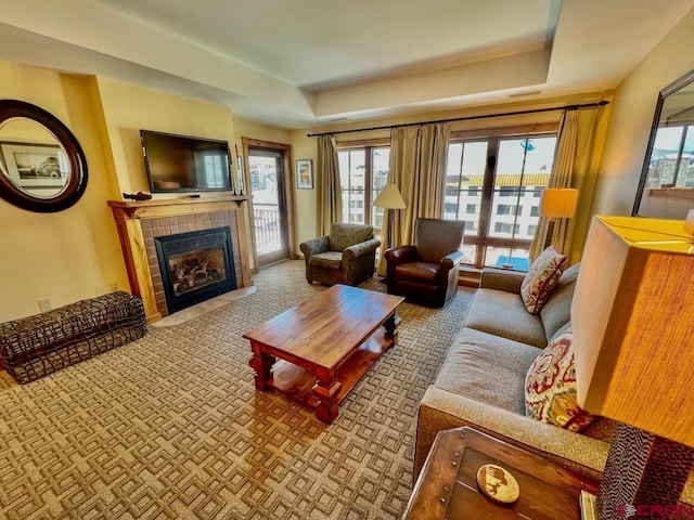 carpeted living room with a tray ceiling and a tiled fireplace