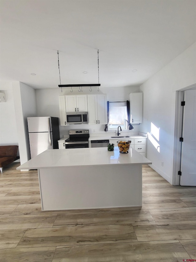 kitchen with white cabinets, appliances with stainless steel finishes, a center island, and light hardwood / wood-style flooring