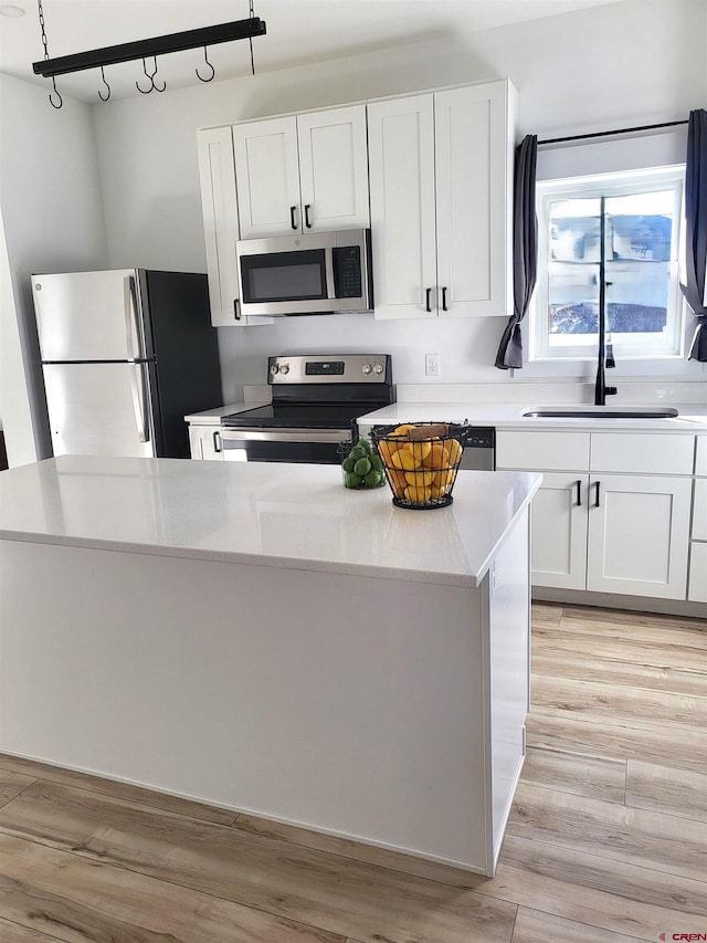 kitchen featuring track lighting, stainless steel appliances, a center island, light hardwood / wood-style floors, and white cabinetry