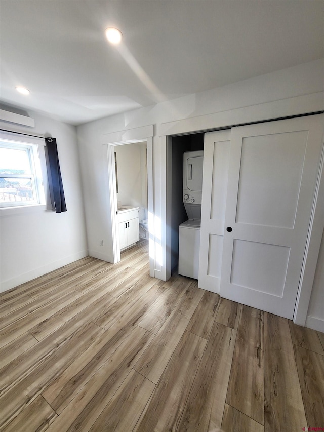 unfurnished bedroom featuring light wood-type flooring, stacked washer and dryer, ensuite bath, and a closet