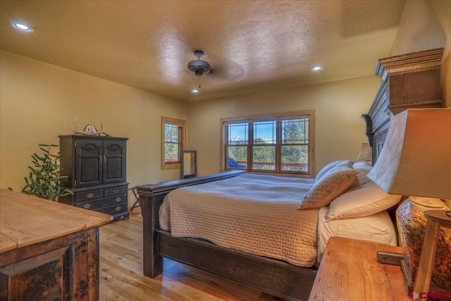 bedroom with ceiling fan, light hardwood / wood-style floors, a textured ceiling, and multiple windows