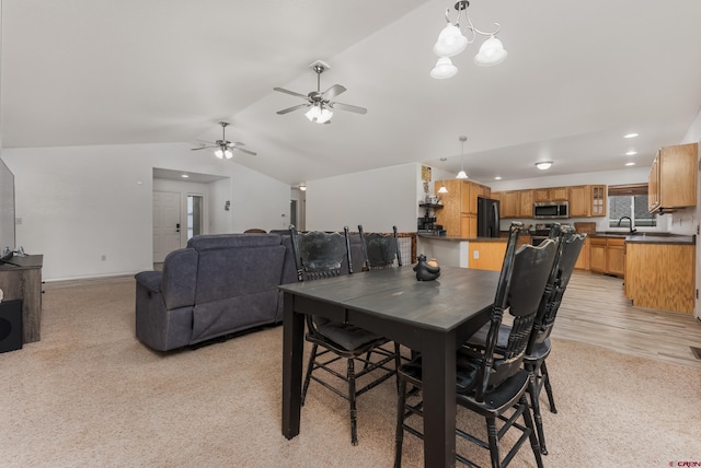 dining room with ceiling fan with notable chandelier, light hardwood / wood-style floors, sink, and vaulted ceiling