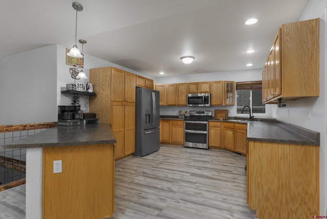 kitchen with kitchen peninsula, appliances with stainless steel finishes, sink, pendant lighting, and light hardwood / wood-style flooring