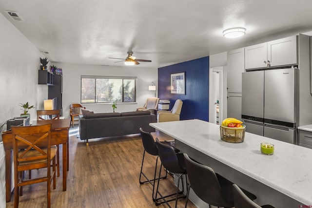 kitchen featuring a breakfast bar, white cabinetry, stainless steel refrigerator, dark hardwood / wood-style floors, and light stone countertops