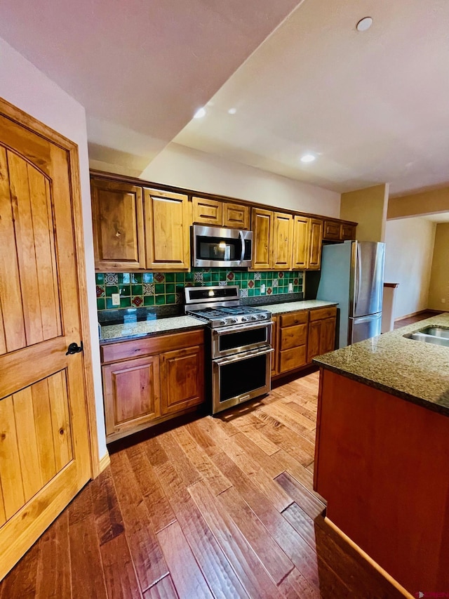 kitchen with appliances with stainless steel finishes, tasteful backsplash, dark stone counters, and wood-type flooring