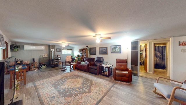 living room with a wood stove, a wall mounted air conditioner, a textured ceiling, and hardwood / wood-style flooring