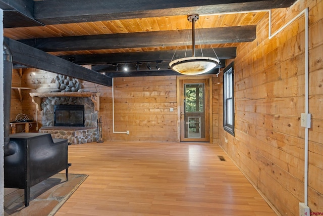 living room with wood walls, a stone fireplace, wood-type flooring, and beam ceiling