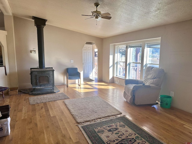 living room featuring a textured ceiling, light hardwood / wood-style floors, a wood stove, and ceiling fan