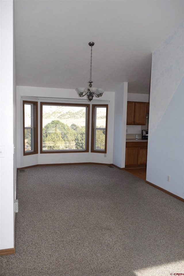 carpeted spare room with a healthy amount of sunlight and an inviting chandelier