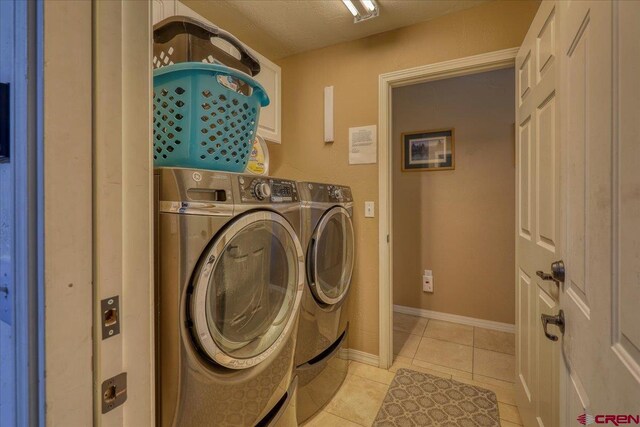 clothes washing area featuring light tile patterned floors, washing machine and dryer, and a textured ceiling