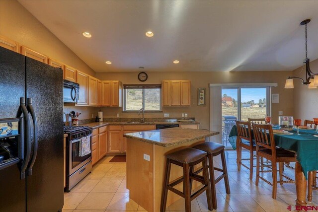 kitchen featuring light brown cabinets, a center island, decorative light fixtures, and black appliances