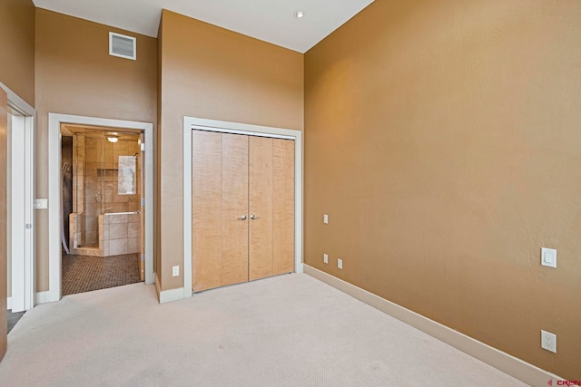 unfurnished bedroom featuring ensuite bathroom, a closet, light colored carpet, and a high ceiling