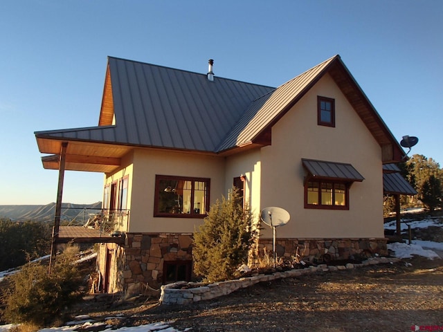 view of side of home featuring stone siding, metal roof, a standing seam roof, a mountain view, and stucco siding