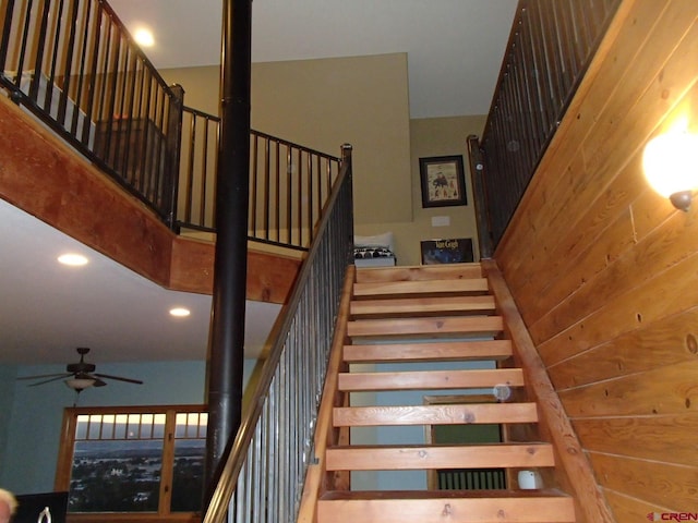 stairs featuring a ceiling fan, recessed lighting, wood walls, and a high ceiling