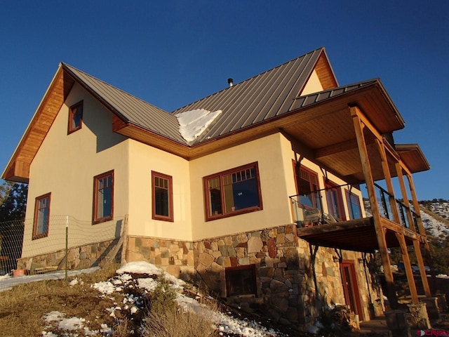 view of snow covered exterior featuring metal roof, a standing seam roof, a balcony, and stucco siding