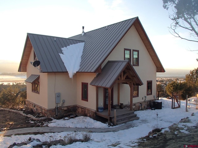 snow covered property featuring metal roof, a standing seam roof, stone siding, and stucco siding