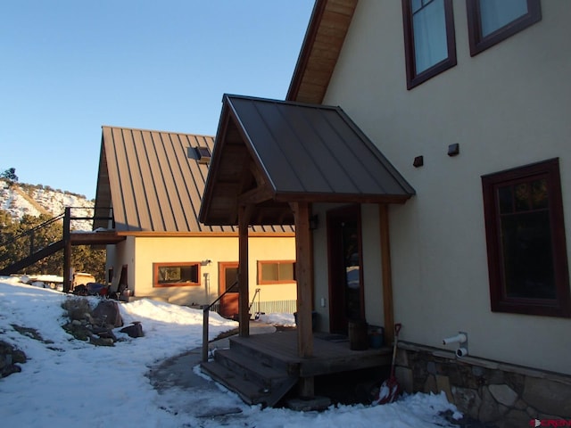 snow covered back of property featuring a standing seam roof, metal roof, and stucco siding