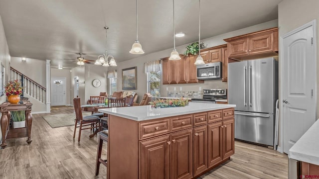 kitchen featuring ceiling fan, a center island, stainless steel appliances, light hardwood / wood-style floors, and decorative light fixtures