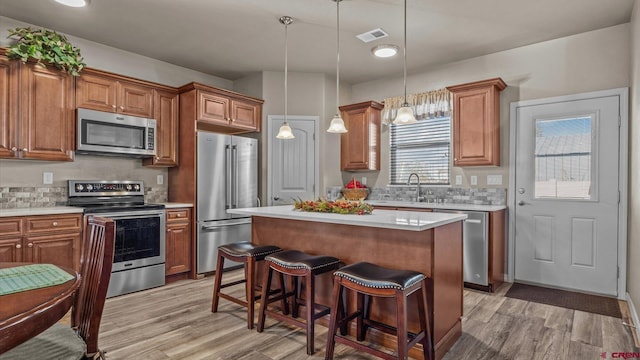 kitchen featuring pendant lighting, a center island, sink, light wood-type flooring, and stainless steel appliances