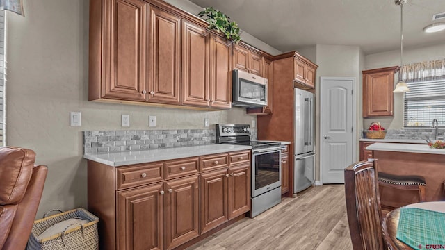 kitchen featuring backsplash, light wood-type flooring, decorative light fixtures, and appliances with stainless steel finishes