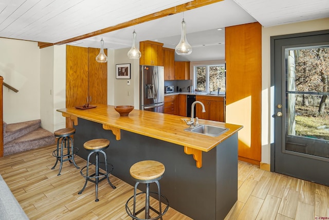 kitchen with a breakfast bar, sink, stainless steel refrigerator with ice dispenser, and light hardwood / wood-style flooring