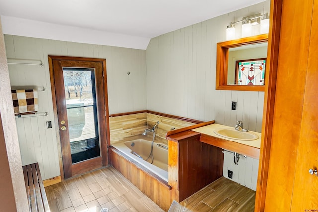 bathroom with lofted ceiling, wooden walls, a bathing tub, and sink