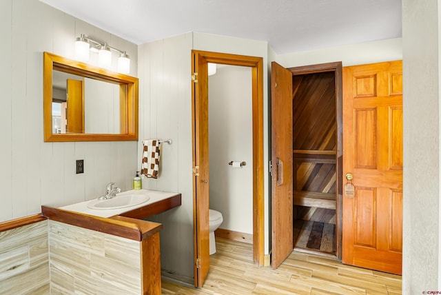 bathroom featuring hardwood / wood-style flooring, toilet, sink, and wooden walls