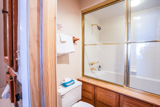 bathroom with toilet and shower / bath combination with glass door