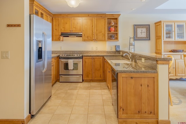 kitchen with light stone countertops, sink, stainless steel appliances, kitchen peninsula, and a breakfast bar area