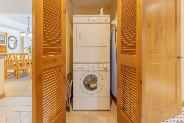 clothes washing area featuring light tile patterned floors, an inviting chandelier, and stacked washer / dryer