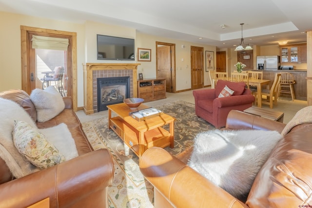 carpeted living room featuring a raised ceiling and a tiled fireplace