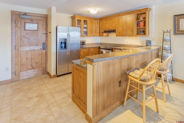 kitchen with a kitchen breakfast bar, light tile patterned floors, kitchen peninsula, and appliances with stainless steel finishes