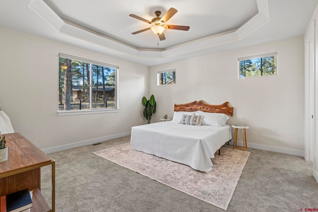 bedroom with ceiling fan, light colored carpet, and a tray ceiling