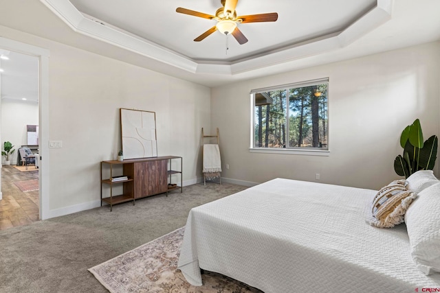 carpeted bedroom with a raised ceiling and ceiling fan